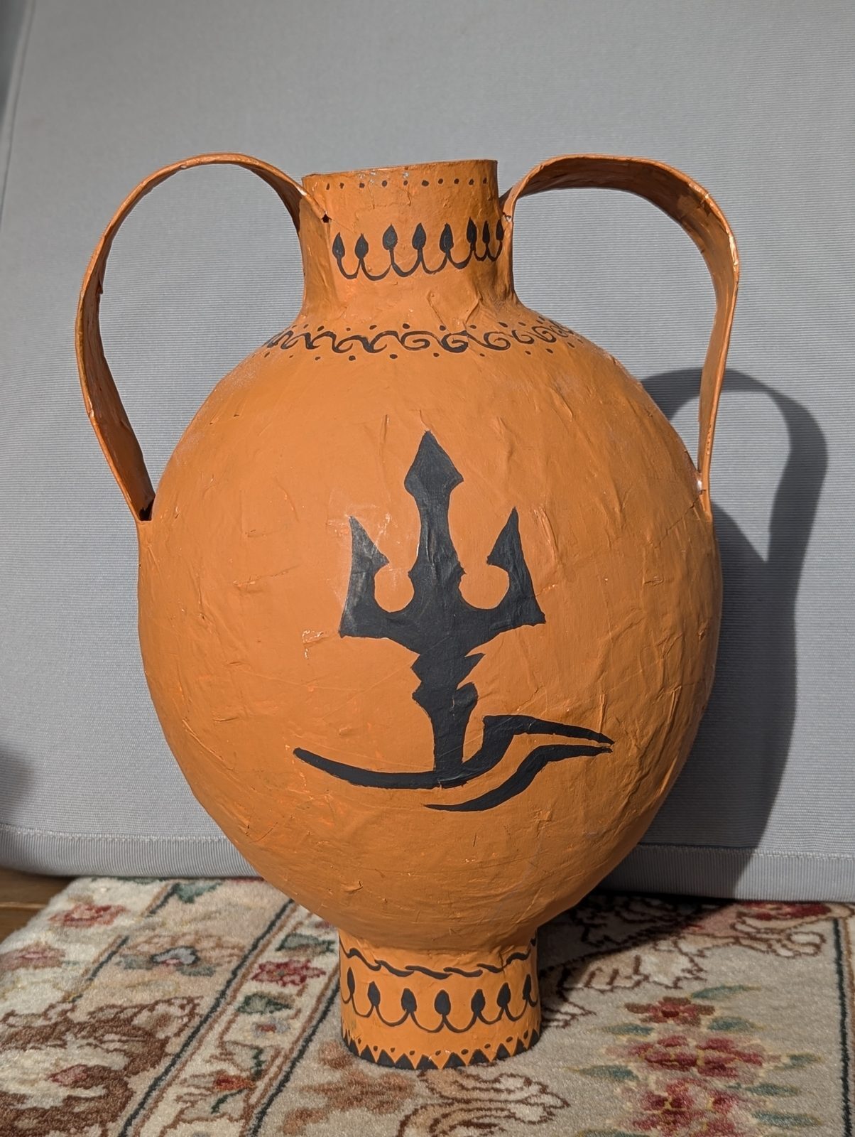 A student-made paper-mâché Greek amphora with a trident design.
